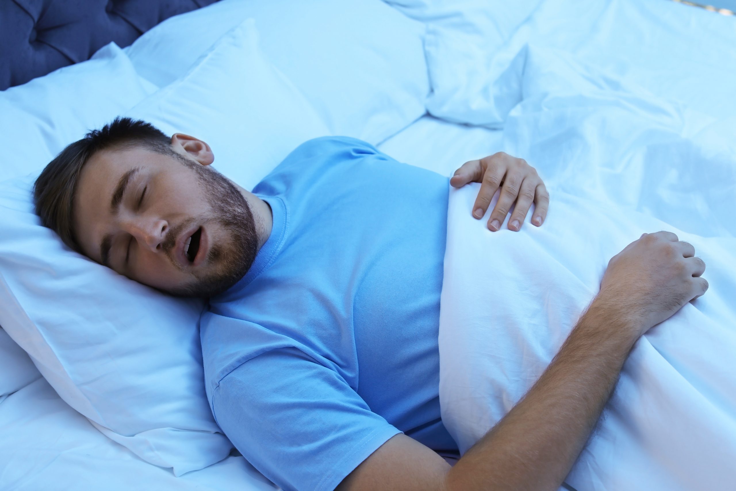 Young man snoring while sleeping in bed at night.