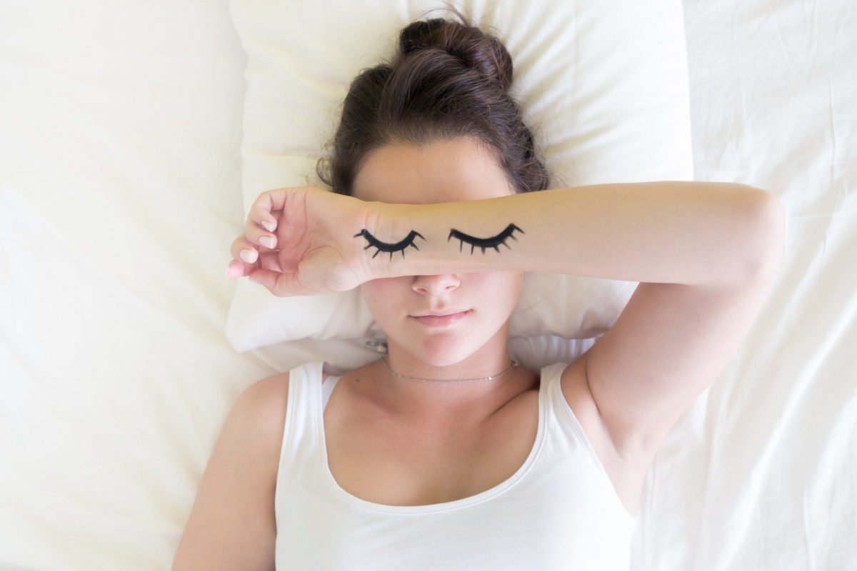 woman laying down with arm over eyes and eyes painted on arm