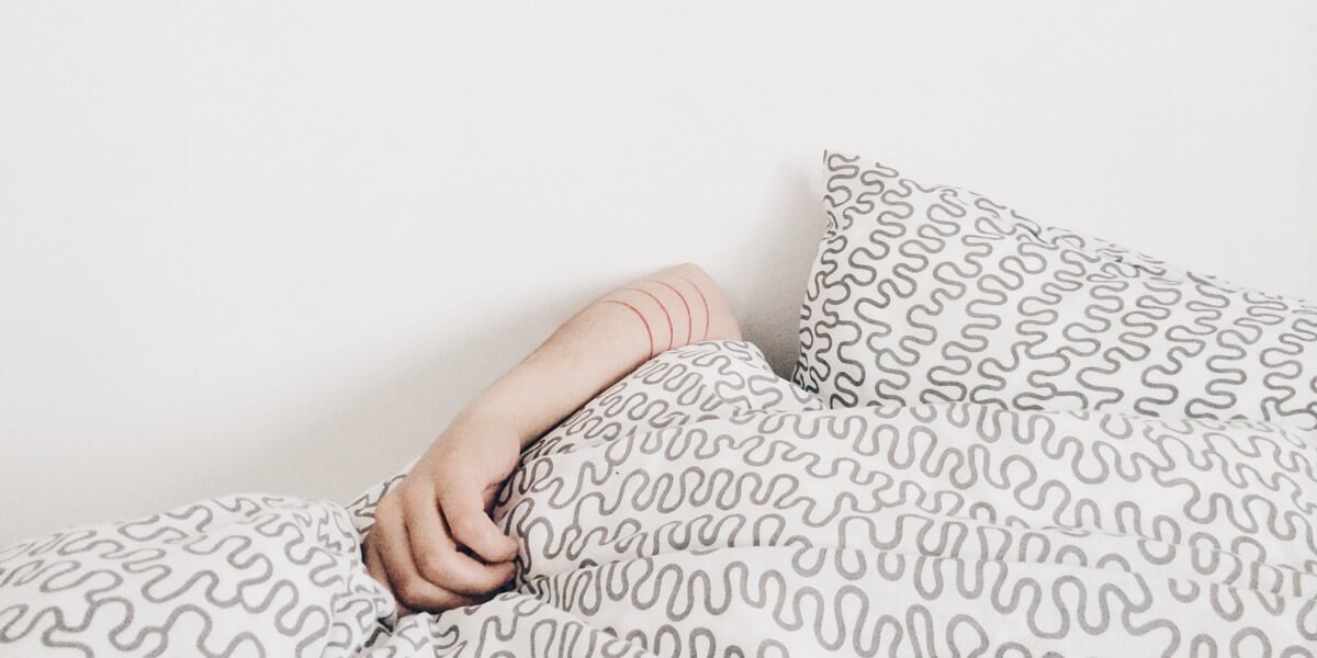 person sleeping with arm hanging out of comforter