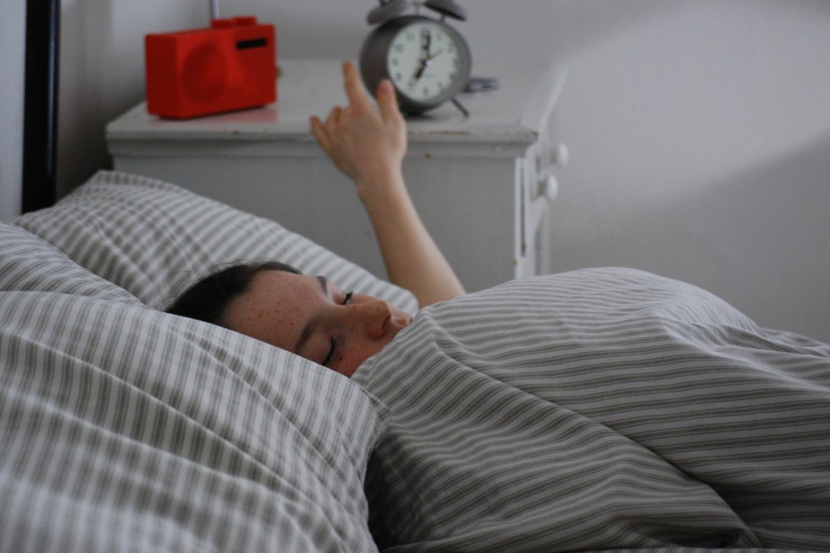 female sleeping in bed hitting alarm clock